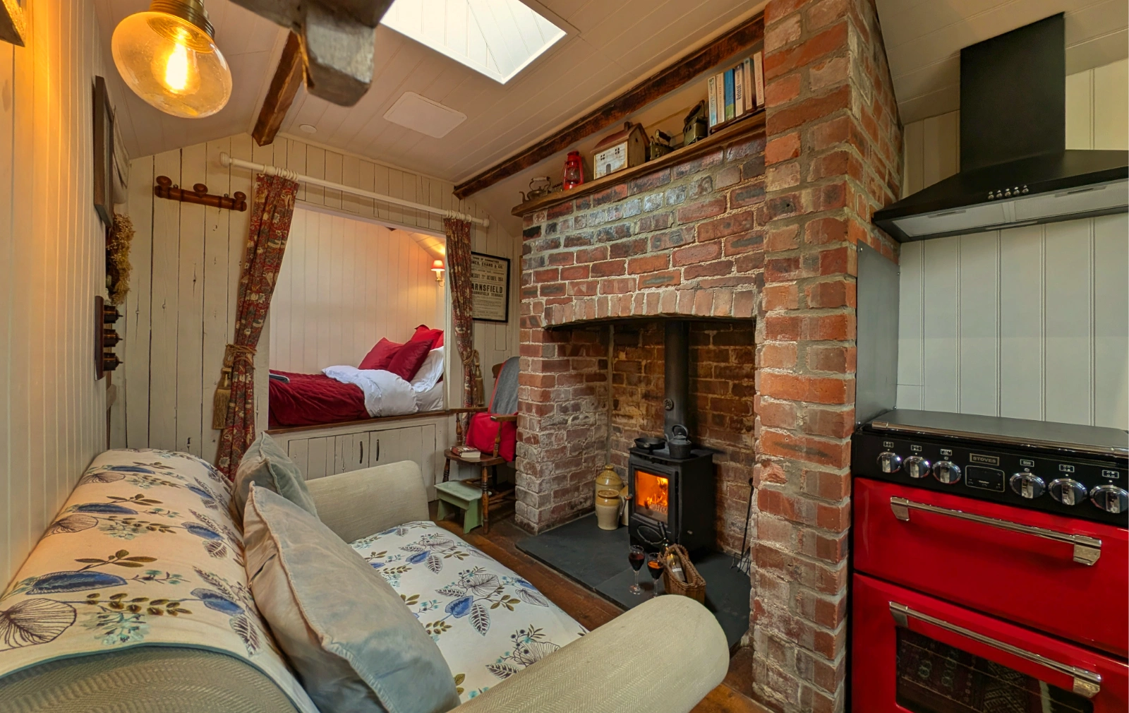 Cosy open-plan interior of Y Golchdy with a wood-burning stove, red range cooker and bedroom nook.