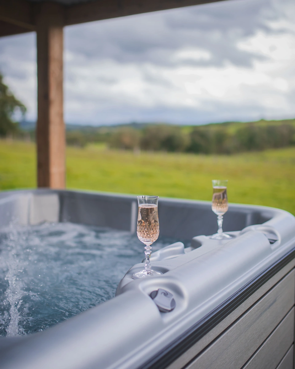 Covered outdoor hot tub at Y Golchdy overlooking the Welsh countryside at golden hour with champagne glasses ready to enjoy.