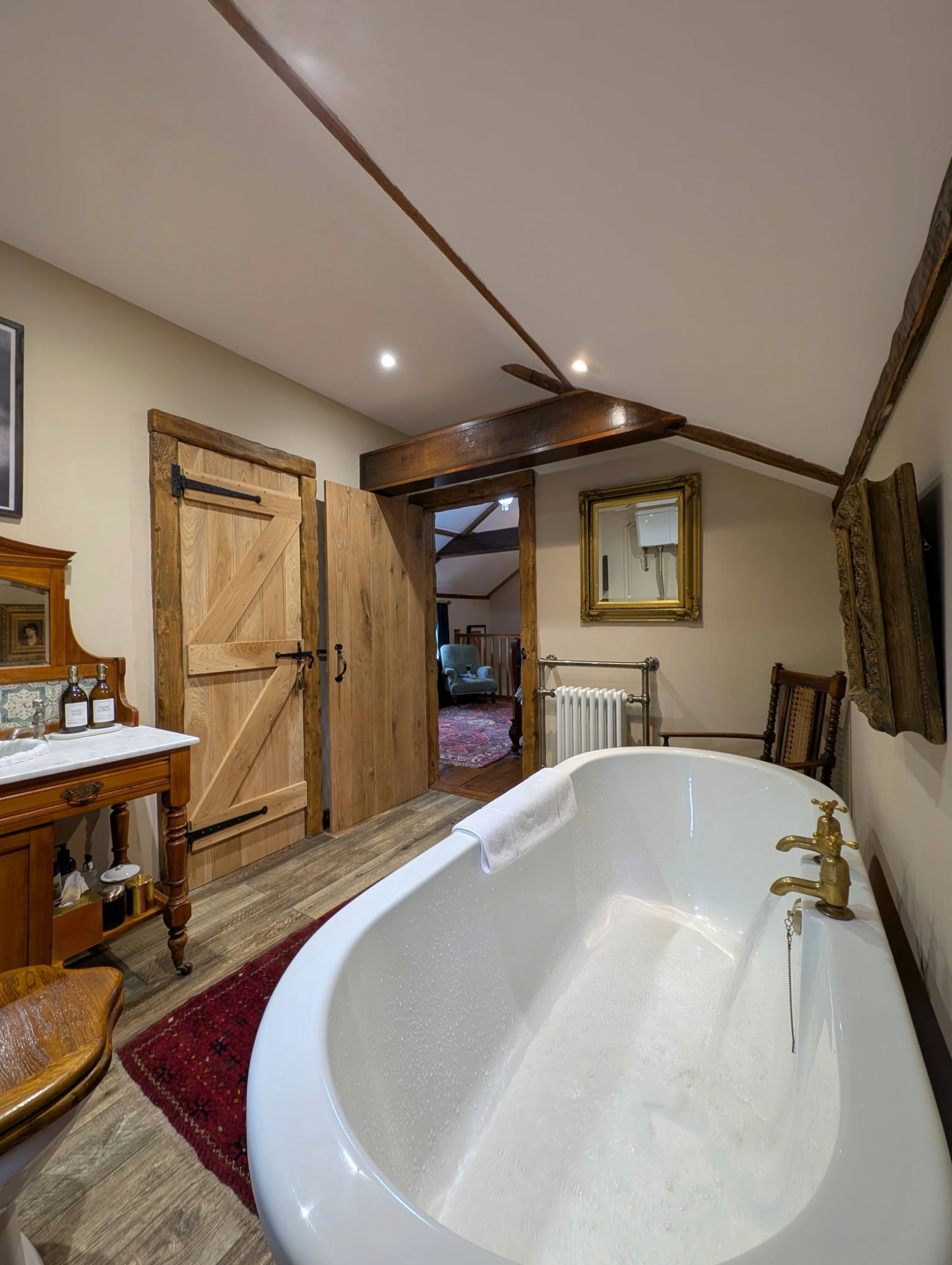 Wide-angle view of the en-suite bathroom at Gablebach Cottage featuring a freestanding roll-top bath and sink vanity unit